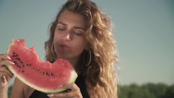 Portrait de femme mignonne avec des cheveux ondulés manger pastèque en plein air Jeune fille aime son repos et sourit — Video