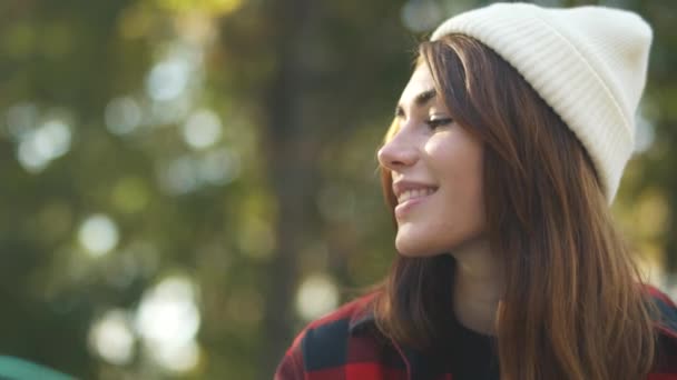 The guy passes the skateboard to the girl in a plaid shirt and white hat. Girl takes a skateboard and hugs her friend while sitting outdoors. — Stock Video