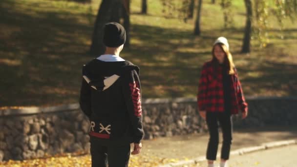 Skateboarder chica en un sombrero blanco y una camisa a cuadros monta un monopatín para el chico y lo abraza en cámara lenta. Pasatiempos y estilo de vida . — Vídeo de stock