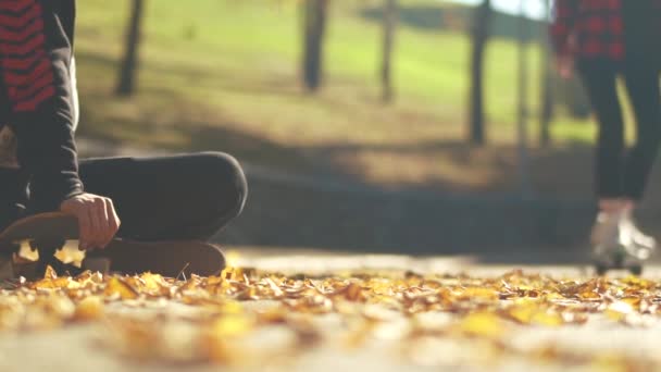 Hipster chega em um skate para o cara e se senta ao lado dele. Adolescentes com skates relaxando ao ar livre. Passatempos e estilo de vida . — Vídeo de Stock