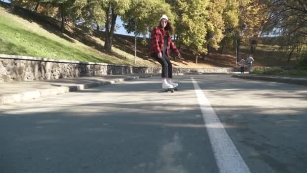 Roztomilý skateboardista dívka v bílém klobouku a kostkovanou košili jezdí na skateboardu venku. Bokovky dívka na koni skate desky hobby a životní styl — Stock video