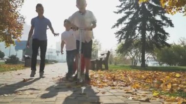 Çocuk ile bir scooter sonbahar parkta gidiyor. Arkadaşlar açık havada bir scooter sürme bir çocukla yetişmeye. Çocuklar parkta oynarken.