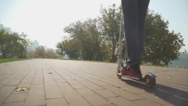 O rapaz monta uma scooter no parque. A câmera se move atrás do  . — Vídeo de Stock