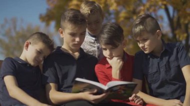 Çocuklar şirket bankta oturan ve bir kitap at binme. Arkadaşlar zaman sürme kitap güneşli bir günde sonbahar parkta geçirmek.