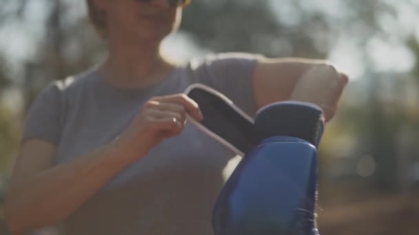 Porträt einer erwachsenen Frau zieht Boxhandschuh aus nächster Nähe an. Weibchen ist glücklich und lächelt. — Stockvideo