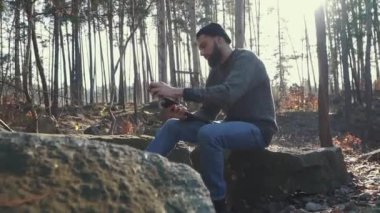 Sakallı adam ormandaki bir balta keskin. Acımasız adam açık havada bir balta ile oturan.