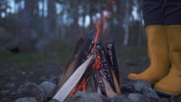Lidské nohy v žluté gumové boty těsné blízkosti hořícího ohně v lese. — Stock video