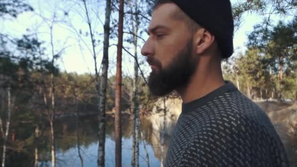 Un uomo barbuto nella foresta che guarda lontano. Un uomo con un'ascia in piedi su una scogliera . — Video Stock