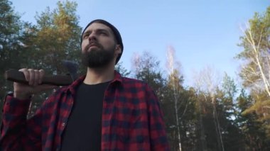 Sakallı adam ormanda elinde bir baltayla duruyor... Acımasız ciddi adam açık havada balta ile.