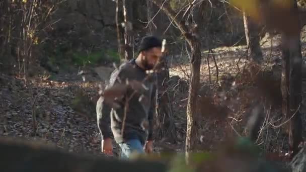 Un hombre caminando por el bosque con hacha en las manos. Joven barbudo camina con un hacha al aire libre . — Vídeo de stock