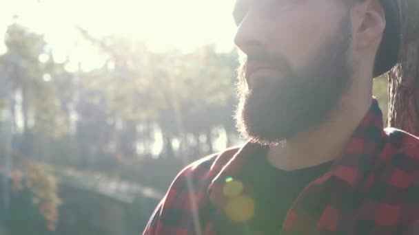 Homme barbu avec une hache à la lumière du soleil à l'extérieur. Brutal homme sérieux se tiennent près de l'arbre avec la hache à la main, pensant . — Video