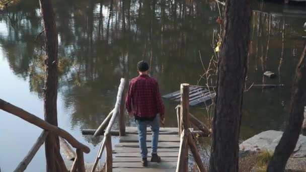 Brutale bebaarde man lopen naar een meer door brug witn een bijl in zijn hand. Young bebaarde man met een bijl buitenshuis. — Stockvideo