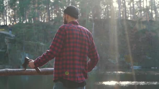 Hombre barbudo con un puesto de hacha en el bosque cerca del lago y lo que sea una vista increíble. Un hombre con un hacha . — Vídeo de stock