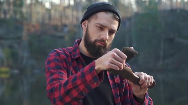Un jeune homme barbu regarde sa hache. Brutal mec sérieux avec hache à l'extérieur . — Video
