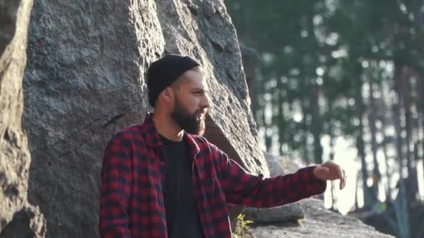 Bearded man stand near huge stone and looking around. Brutal serious guy with ax outdoors. — Stock Video
