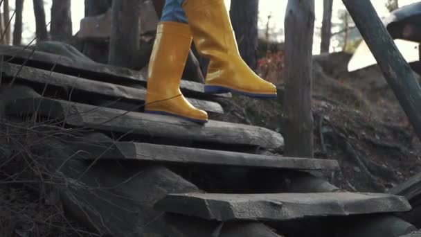 Les jambes humaines en bottes en caoutchouc jaune et en jeans bleus descendent les escaliers en bois à l'extérieur. Pieds dans des bottes en caoutchouc descendant un escalier en bois dans la forêt . — Video