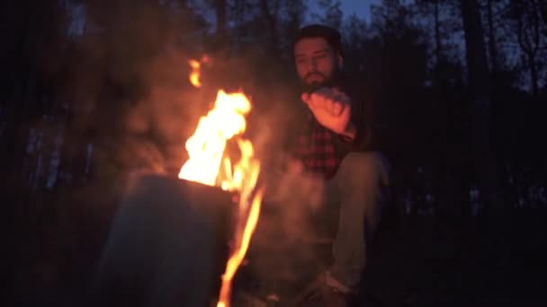 Een beadred man zitten in de buurt vreugdevuur en warmimg zijn handen in het bos in duisternis. Woodman door de brand in het bos. — Stockvideo