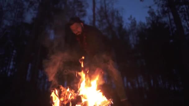 Бородатий чоловік нарізає палаючий колоду вночі в лісі. Жорстокий хлопець з сокирою на відкритому повітрі . — стокове відео
