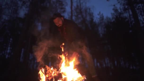 Un barbu coupant une bûche brûlante la nuit dans la forêt. Brutal gars avec hache à l'extérieur . — Video