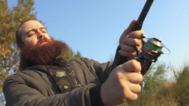 Sakallı adam bir olta ile Balık tutma. Balıkçı balık çekerek bir iplik bobin açar.