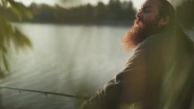 Nehir kıyısında oturan balık uzun sakallı Balıkçı yakalar. Fisher arkadaşı onun el greetiings el salla. Nehir Balık tutma.