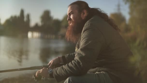 Vousatý rybář loví na břehu řeky. Fisher kouří cigarety venku. Říční rybolov. — Stock video