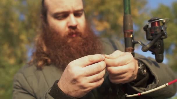 Pêcheur met un ver sur le crochet et pointe sur elle. Portrait d'un homme adulte avec barbe mettant un aileron sur le crochet. Pêche à l'appât vivant. Pêche sur la rivière . — Video