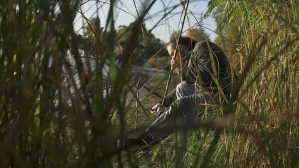 Visser is de vaststelling van zijn spinnen die zittend op de bank van de rivier. De man is betrokken bij een visserij. — Stockvideo