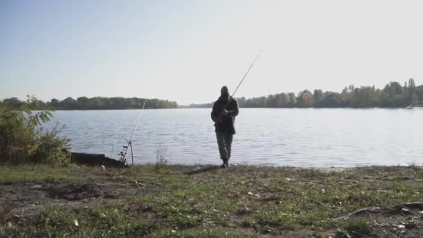 Γενειοφόρος ψαράς περνούν από τη φωτογραφική μηχανή με καλάμι. Ο άνθρωπος εμπλέκεται σε ένα χόμπι. Ψάρεμα σε ποτάμι. Αργή κίνηση. — Αρχείο Βίντεο