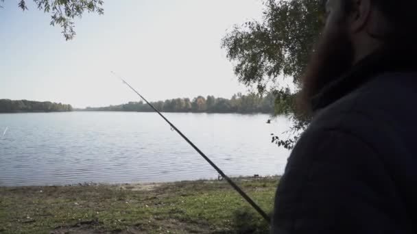 Pêcheur se tient debout avec une canne à pêche sur la rive de la rivière et regarde l'eau et un oiseau volant au-dessus de l'eau. Mouvement lent . — Video