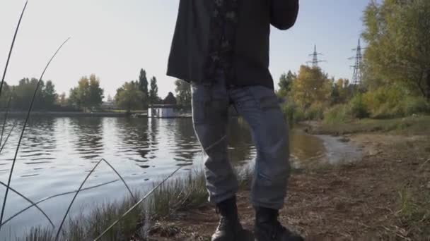 Pescador con barba larga se estira en la orilla del río con cañas de pescar. El hombre mira a lo lejos, cubriéndose los ojos con la mano del sol. Movimiento lento . — Vídeo de stock