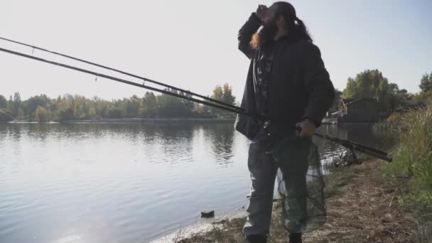 Pescador solitario con largas barbas pasea por la orilla del río con cañas de pescar. Movimiento lento . — Vídeo de stock