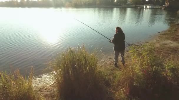 El pescador está pescando en la orilla del río bajo el sol. Barbudo pescando desde la orilla con buen tiempo . — Vídeo de stock