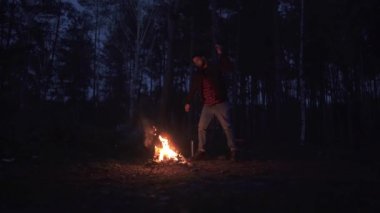 Yanan bir günlük gece ormanda doğrama sakallı adam. Acımasız adam açık havada balta ile.