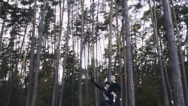 Молодая пара танцует в лесу на фоне прекрасных сосен. Влюбленная межрасовая танцующая пара. Парень кружится со своей девушкой, держащей ее на руках. Гибкая кавказская девушка — стоковое видео