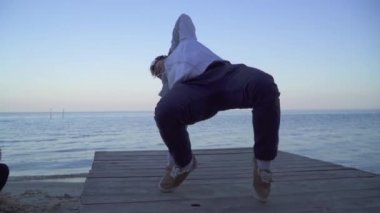 Asya yakışıklı olan nehir kıyısında güzel beyaz kız önünde dans break dans rahat kıyafetler içinde. Asya adam dans breakdance açık havada. Sevimli gülümseyen kız sevgilisini görünüyor