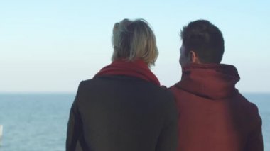 Açık havada birlikte vakit genç neşeli ırklararası çift. Asya'ya ait adam ve rahat kıyafet ayakta su yüzeyi arka plan üzerinde beyaz kız. Adam kıza ile işaret eden bir şey gösterir