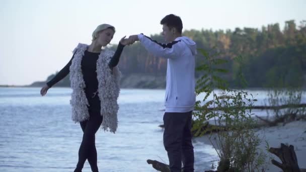 Tonåringar i fritidskläder som dansar på sandstranden flodbank. Interracial par Dans i fri stil utomhus. Asiatisk kille och kaukasiska flicka dansa modern dans. Slow motion. — Stockvideo