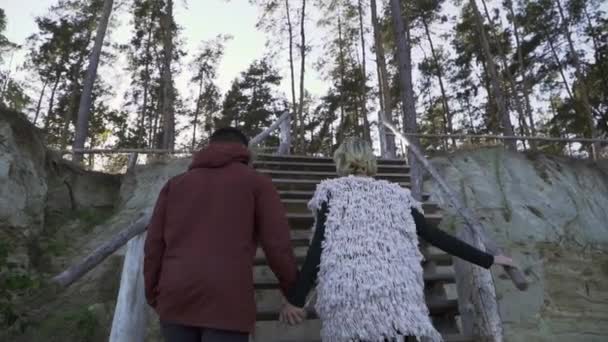 Der junge Mann und das Mädchen halten die Hand und steigen die Holztreppe hinauf. junges Paar verbringt Zeit zusammen im Freien. Paar verbringt Zeit außerhalb der Stadt. — Stockvideo