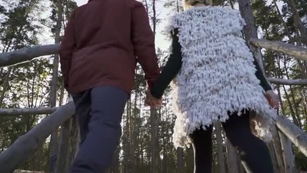 Young guy and the girl hold the hands and climb the wooden stairs and walk through the forest. Young couple spends time together outdoors. A couple spends time out of town. Slow motion. — Stock Video