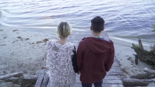 El joven y la chica toman la mano y bajan las escaleras de madera. Pareja joven pasa tiempo juntos al aire libre. Una pareja pasa tiempo fuera de la ciudad . — Vídeos de Stock