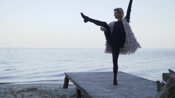 Гнучка дівчина танцює на дерев'яній платформі на фоні поверхні води. Красива молода біла жінка в повсякденному одязі танцює сучасний танець на відкритому повітрі . — стокове відео