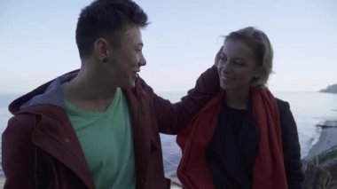 İhale ırklararası çift su yüzeyi arka plan üzerinde konuşurken aşık. Doğada eğlence harcamaları genç etnik insanlar. Asya'ya ait adam açık havada onun kız arkadaşı yanak vuruş.