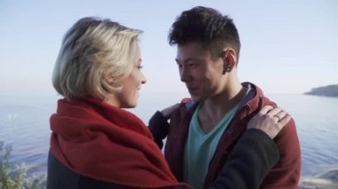 İki aşk bir arka plan bir uçurum, çam ağaçları ve bir göl üzerinde öpüşme sonra gülümseyen genç çok etnik. Öpücük ırklararası çift açık havada.