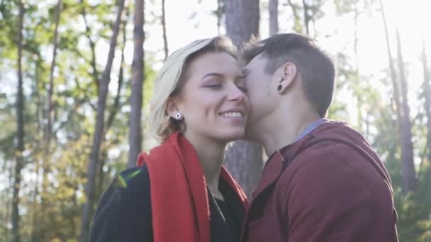 Joven pareja sonriente en el amor besándose en un fondo de pinos y la luz del atardecer. Multi pareja étnica en el amor . — Vídeo de stock