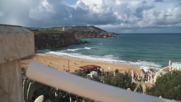 Amazing views of the beach in Malta. Beautiful sandy beach, small hills and cacti growing in the foreground near the hotel terrace. Rain clouds over the sea and the Mediterranean town standing on a — Stock Video