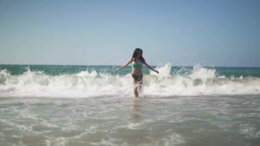 Siyah saçlı ve mükemmel vücut güneş gözlüğü ve bikini giyen güzel kadınla dalga deniz uzak çalışır. Sevimli genç bebek mutlu ve gülümseyen bir tatil tatil beldesinde zevk 's. Ağır çekim.