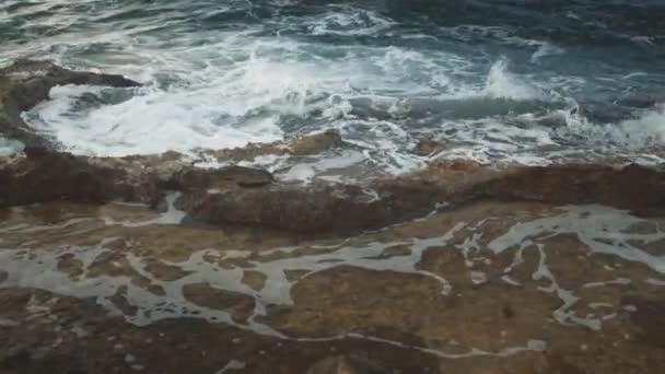 Ondas espumosas a cair numa costa rochosa. Salpicos de uma onda do mar espalham-se nos lados . — Vídeo de Stock