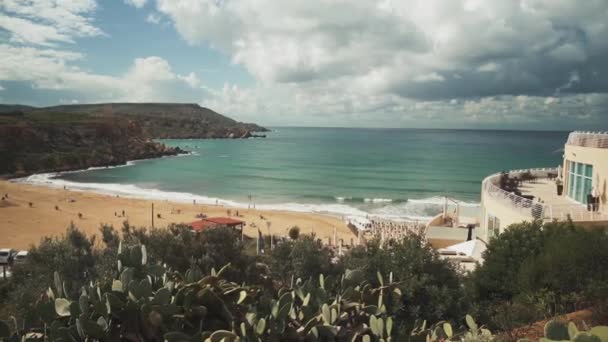 Hermosa vista de la playa de arena en una isla en el Mediterráneo. Nubes de lluvia sobre el mar y la ciudad mediterránea de pie sobre un pequeño acantilado rocoso . — Vídeos de Stock