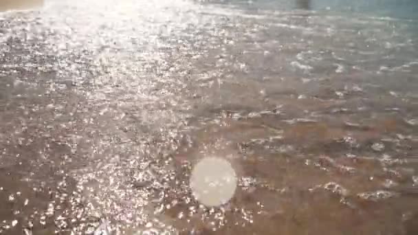 Im Sonnenlicht glitzernde schäumende Meereswellen rollen ruhig über den Sandstrand. Seewellen wälzen sich nacheinander über die sandige Küste. — Stockvideo